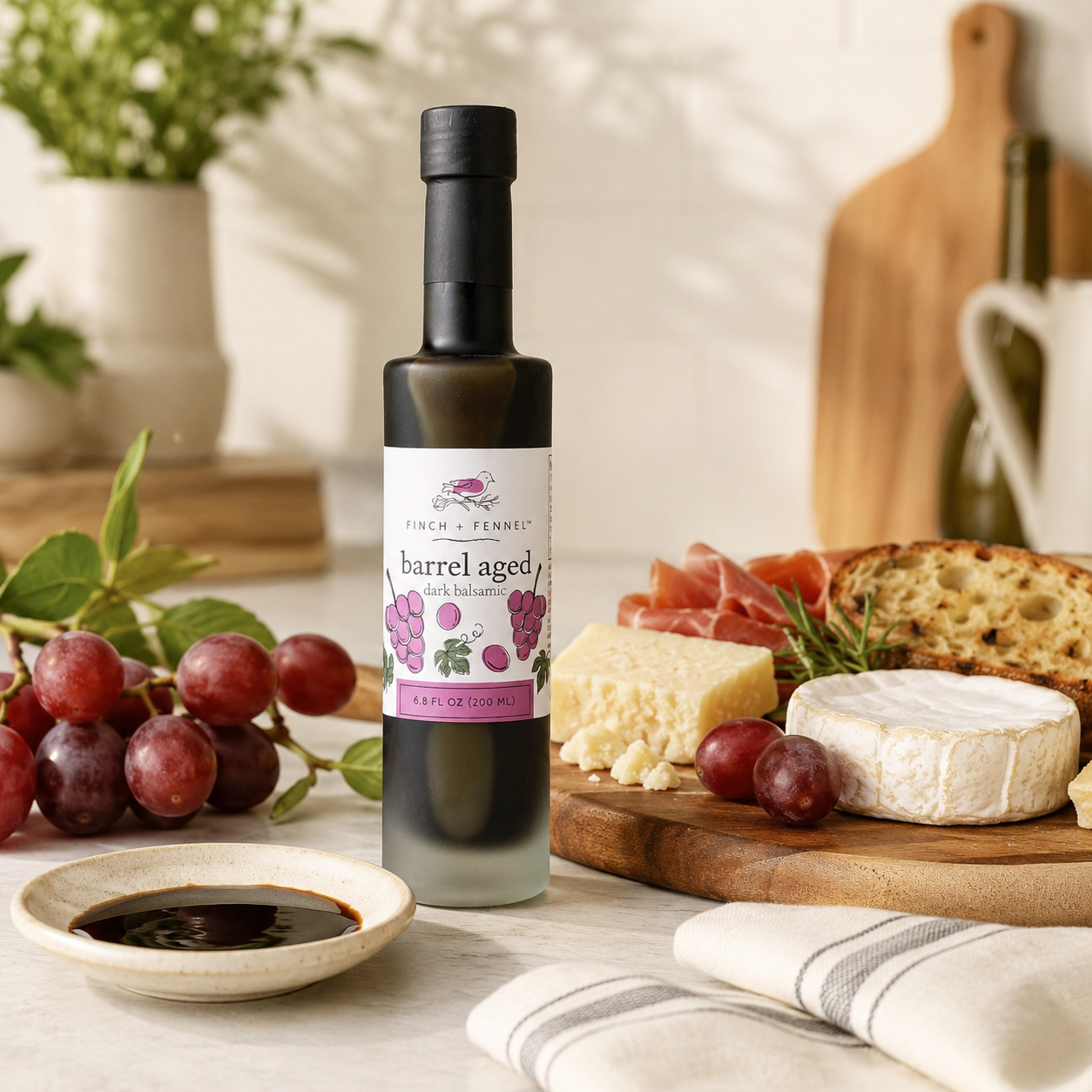 Bottle of barrel-aged dark balsamic vinegar on a table with grapes, cheese, and cured meats.