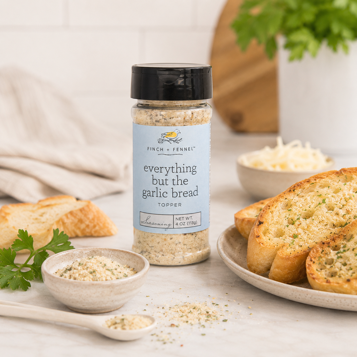Spice jar labeled 'everything but the garlic bread' on a table with garlic bread and ingredients.